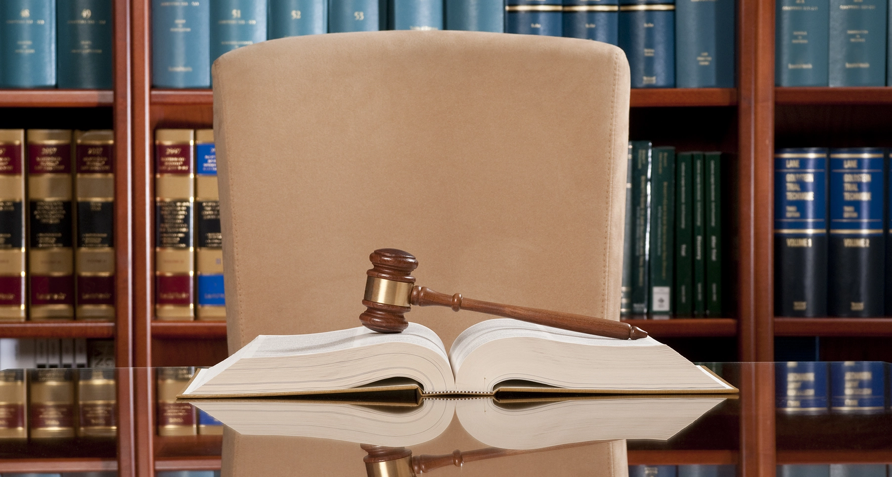 A gavel on top of a legal book with more legal books on shelves in the background.