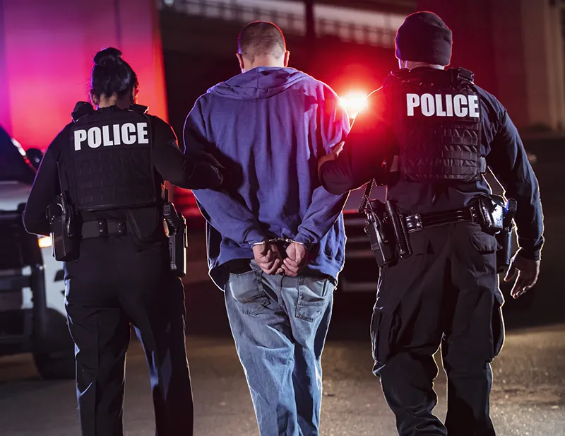 Police escort a handcuffed man who could use Southwest Michigan criminal defense lawyers.