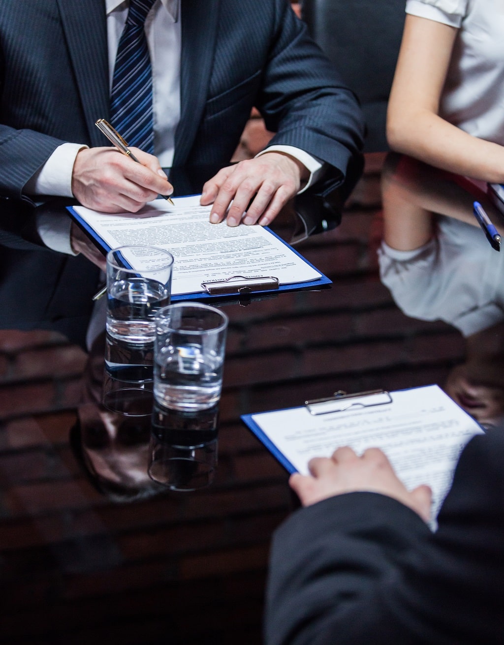 A businessman and businesswoman sign an agreement at a table with another businessman across from them.